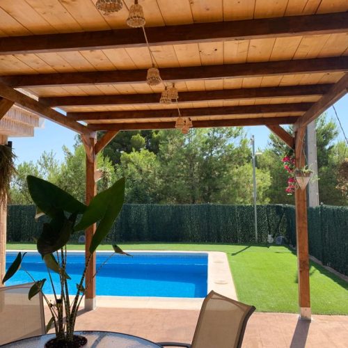 Pérgola de madera laminada  techada con anclajes al suelo incluidos, diseñada para instalaciones exteriores que requieren máxima estabilidad. Estructura robusta con postes y vigas de sección reforzada, tratada para exterior color roble claro, para resistir humedad, sol y cambios climáticos. La cubierta superior proporciona sombra total y protección frente a lluvia ligera. Incluye anclajes metálicos para fijación segura al suelo, garantizando una instalación firme, profesional y de larga durabilidad. Ideal para jardines, terrazas y proyectos de eventos y bodas. Fabricada en España.