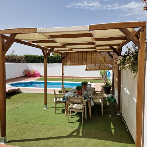 Pérgola de madera maciza tratada en autoclave con toldo fijo de tela beige repelente al agua, diseñada para ofrecer una zona de sombra estable, elegante y duradera en exteriores. La madera, protegida mediante tratamiento en autoclave, garantiza alta resistencia frente a humedad, hongos e inclemencias climáticas. El toldo fijo beige, confeccionado en tejido técnico repelente al agua, aporta protección solar eficaz y resistencia a lluvia ligera. Una solución robusta, estética y de bajo mantenimiento ideal para jardines, terrazas y proyectos de bodas y eventos.